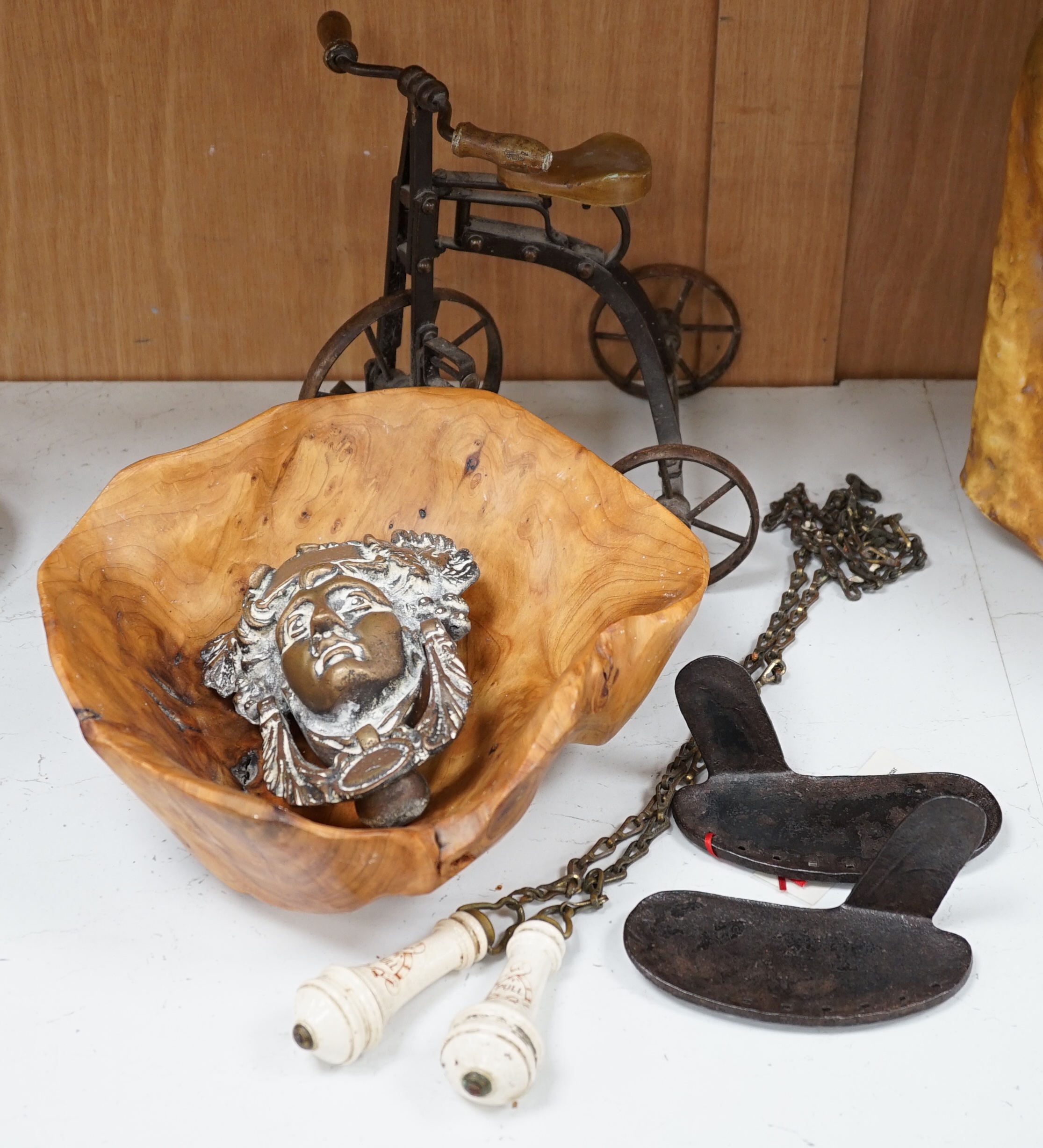 A cast iron toy model of a tricycle, a carved wooden bow, a classical figurative door knocker, a pair of metal cow shoes and two ceramic cistern pulls, bowl 30cm diameter. Condition - fair